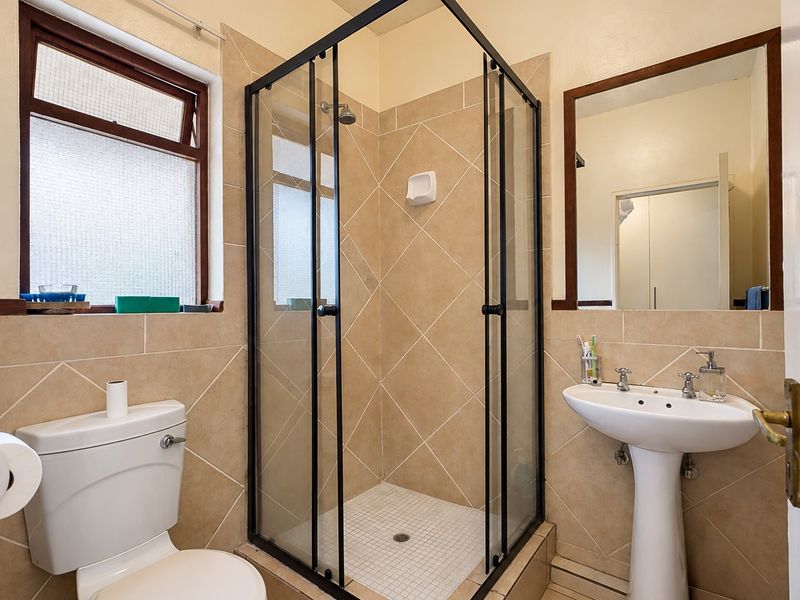 A functional bathroom featuring a shower enclosure, pedestal basin, toilet, and tiled finishes, providing a practical and well-maintained space.