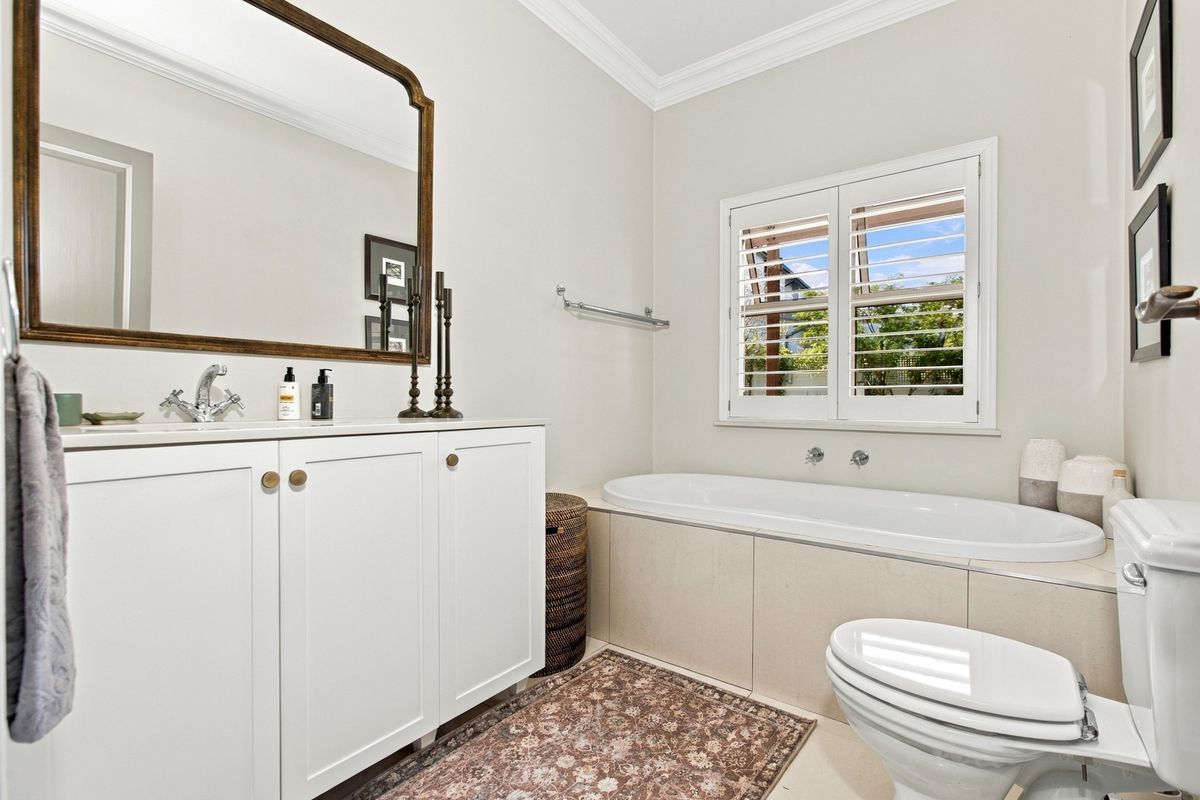 A well-maintained bathroom featuring a built-in vanity, a drop-in bathtub with tiled surround, and plantation shutters for natural light.
