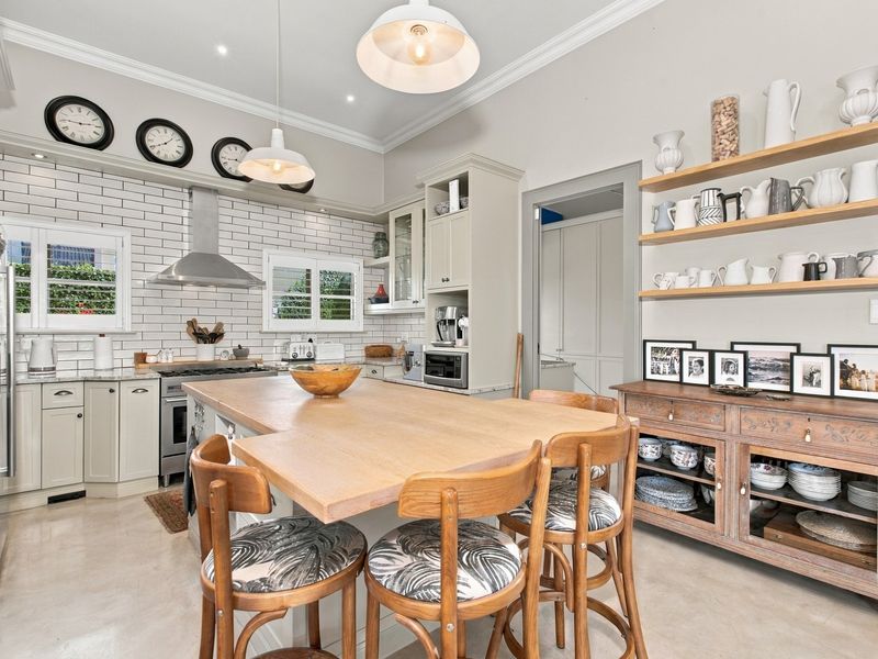 A well-appointed kitchen featuring a central island, subway tile backsplash, stainless steel extractor fan, and ample built-in cabinetry with open shelving.