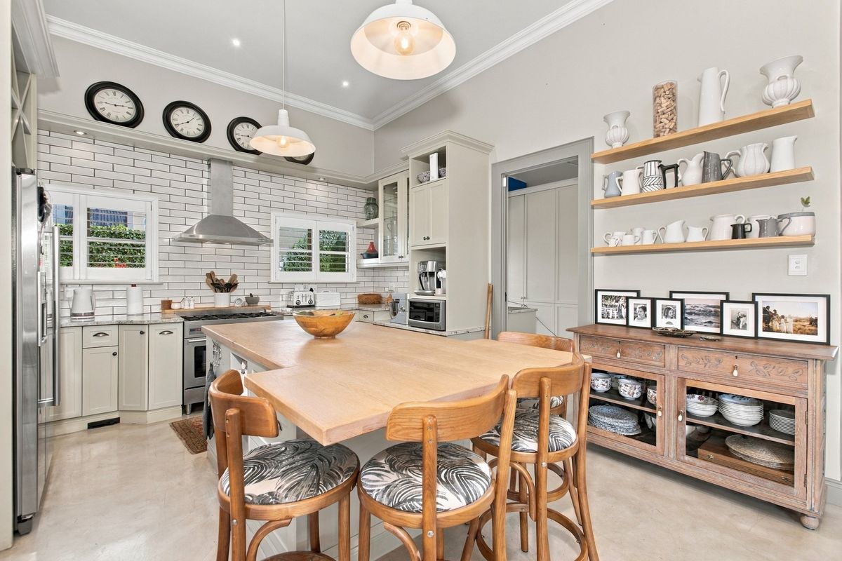A well-appointed kitchen featuring a central island, subway tile backsplash, stainless steel extractor fan, and ample built-in cabinetry with open shelving.