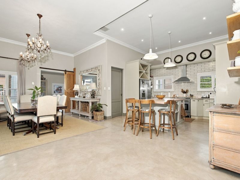 Spacious open-plan living area featuring a modern kitchen with a central island, subway tile backsplash, and polished concrete floors, seamlessly connected to the dining space.