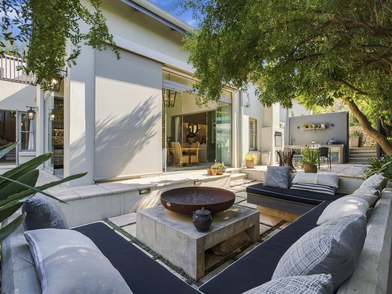 A beautifully landscaped outdoor patio featuring built-in concrete seating, a central fire pit, and a built-in braai area, seamlessly connected to the interior living space.