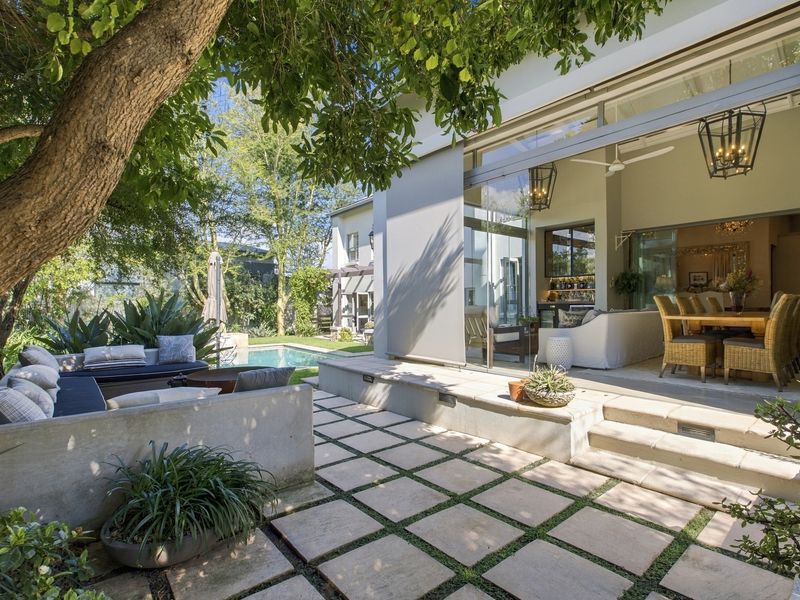 A beautifully landscaped outdoor patio featuring built-in concrete seating, stone paving, and seamless indoor-outdoor flow through large retractable glass doors overlooking the pool area.