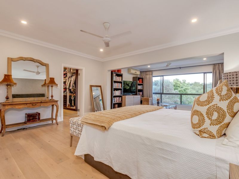 Spacious bedroom featuring light timber flooring, recessed lighting, a ceiling fan, and an integrated walk-in closet with large windows overlooking greenery.