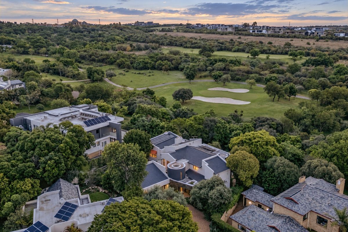 Aerial view of a residential property featuring solar panels, tiled roofing, and lush surrounding greenery overlooking a golf course.