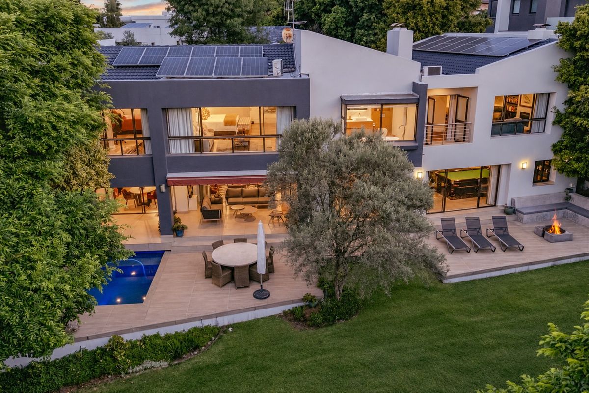 Aerial view of a modern two-story residence featuring a swimming pool, expansive tiled patio, built-in fire pit, and rooftop solar panels.