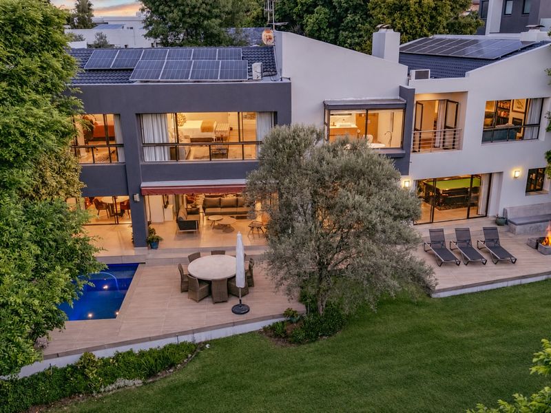 Aerial view of a modern two-story residence featuring a swimming pool, expansive tiled patio, built-in fire pit, and rooftop solar panels.