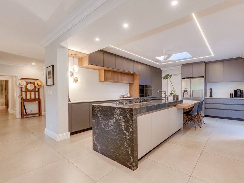 Modern open-plan kitchen featuring a large stone-topped island, sleek cabinetry, integrated appliances, recessed lighting, and a skylight, creating a bright and functional culinary space.