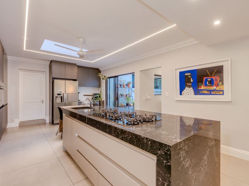 Modern kitchen featuring a large island with a stone countertop, integrated gas hob, sleek cabinetry, recessed lighting, and a skylight for natural illumination.