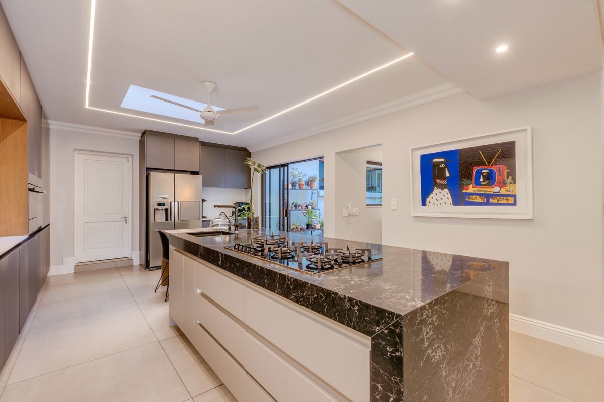 Modern kitchen featuring a large island with a stone countertop, integrated gas hob, sleek cabinetry, recessed lighting, and a skylight for natural illumination.