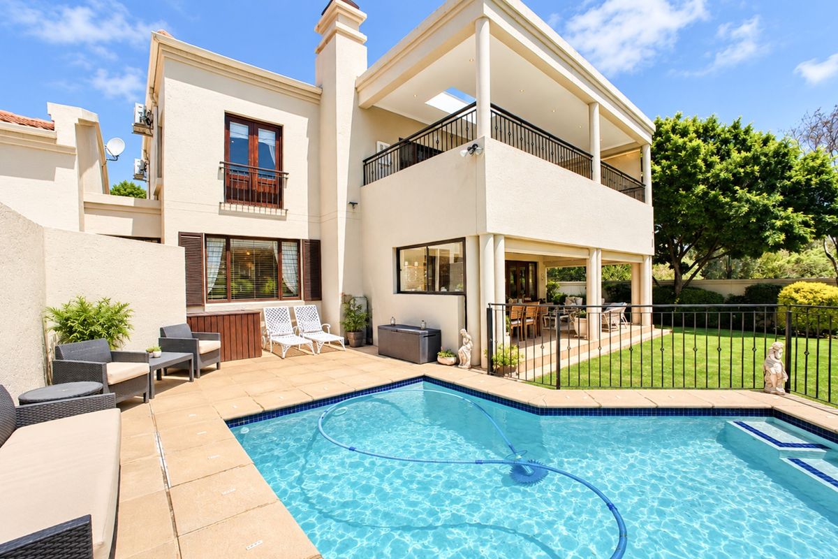 Rear view of a two-story residence featuring a swimming pool, paved patio area, and a covered balcony overlooking the garden.