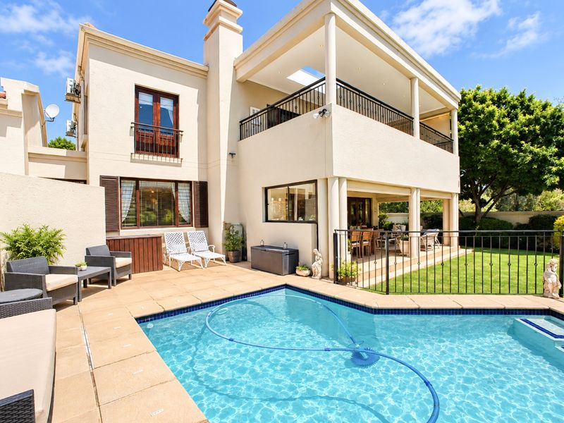 Rear view of a two-story residence featuring a swimming pool, paved patio area, and a covered balcony overlooking the garden.