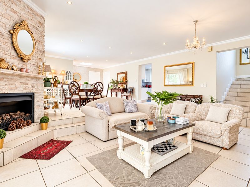 Spacious open-plan living area featuring a prominent stone-clad fireplace, tiled flooring, and a split-level layout leading to a dining space and staircase.