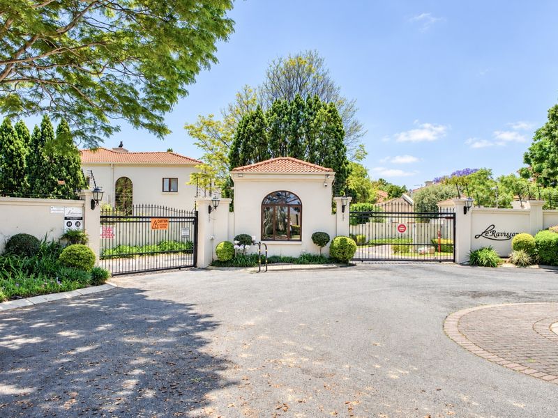 The secure gated entrance to Le Ravissant estate, featuring a guard house, perimeter walls with electric fencing, and a well-maintained paved driveway.