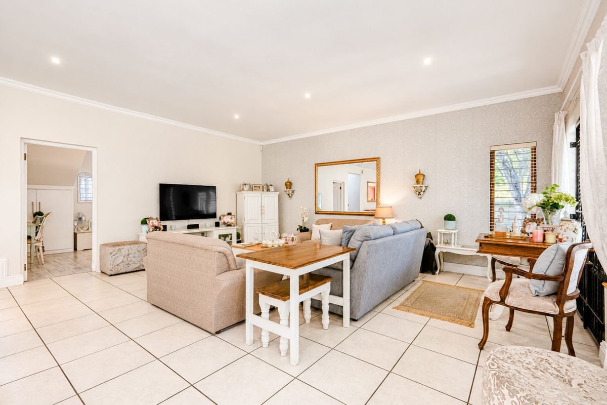 A well-maintained living room featuring neutral tiled flooring, recessed downlighting, and decorative textured wallpaper, offering a bright and comfortable living space.