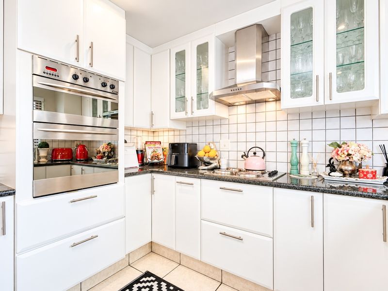 A well-maintained kitchen featuring white cabinetry, granite countertops, a tiled backsplash, and integrated stainless steel appliances including an oven and extractor fan.