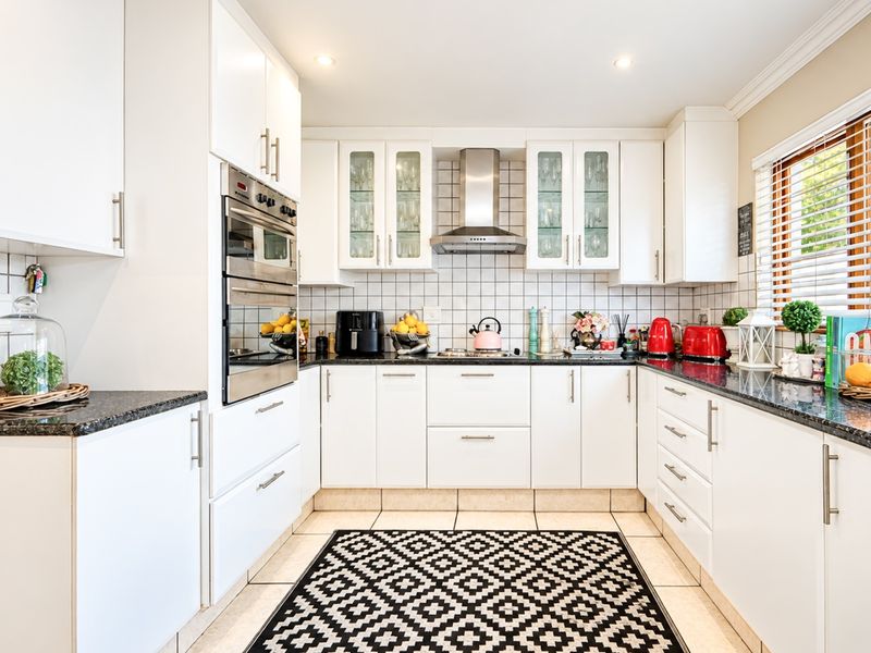 A well-maintained kitchen featuring white cabinetry, granite countertops, a built-in oven, and a stainless steel extractor fan with a classic tiled backsplash.