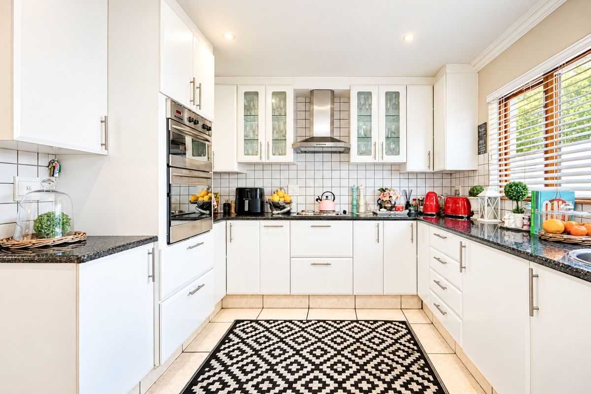 A well-maintained kitchen featuring white cabinetry, granite countertops, a built-in oven, and a stainless steel extractor fan with a classic tiled backsplash.