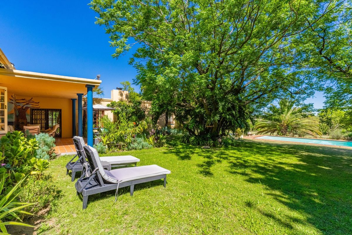 A spacious rear garden featuring a covered patio, lush lawn, mature trees, and a swimming pool, offering a serene outdoor living space.