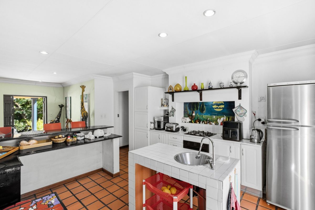 A functional kitchen featuring white cabinetry, a tiled island with a sink, gas hob, and a breakfast bar overlooking the living area.