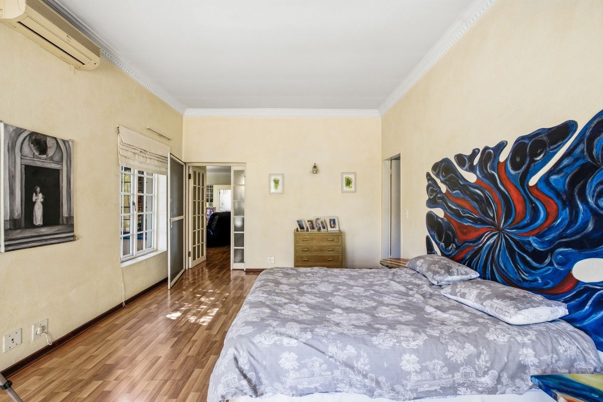 Spacious bedroom featuring laminate flooring, crown molding, and a wall-mounted split-system air conditioner, with access through classic french doors.
