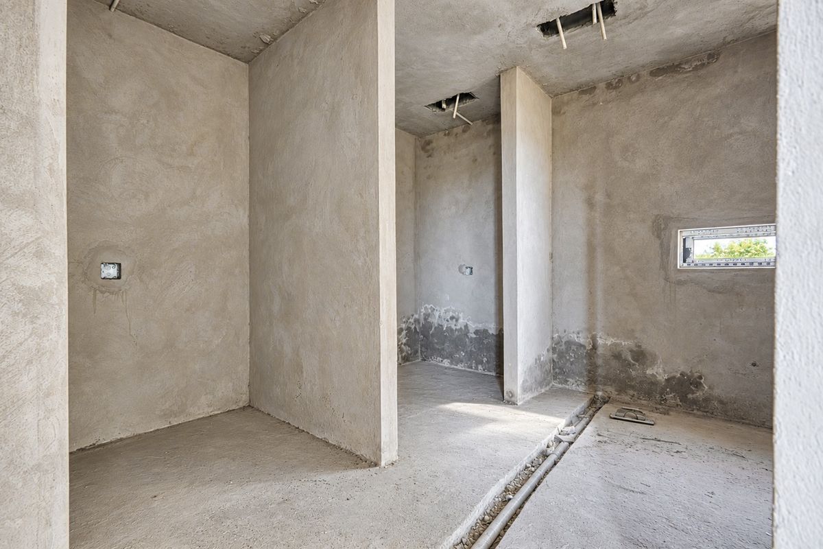 An unfinished bathroom space in shell condition, featuring exposed plumbing and electrical rough-ins, ready for final tiling and fixture installation.