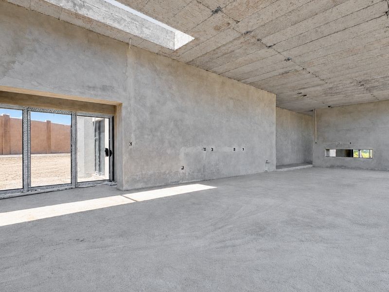Spacious open-plan interior in shell condition featuring exposed concrete ceilings, large sliding glass doors, and a skylight, offering a blank canvas for custom finishes.