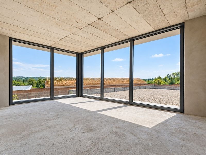 An unfinished living space featuring exposed concrete ceilings, concrete floors, and expansive floor-to-ceiling windows with views of the surrounding area.