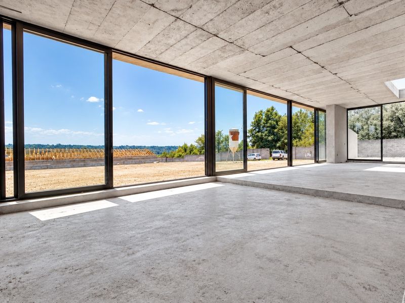An expansive, unfinished living area featuring raw concrete ceilings and floors with large sliding glass doors offering panoramic views of the surrounding landscape.