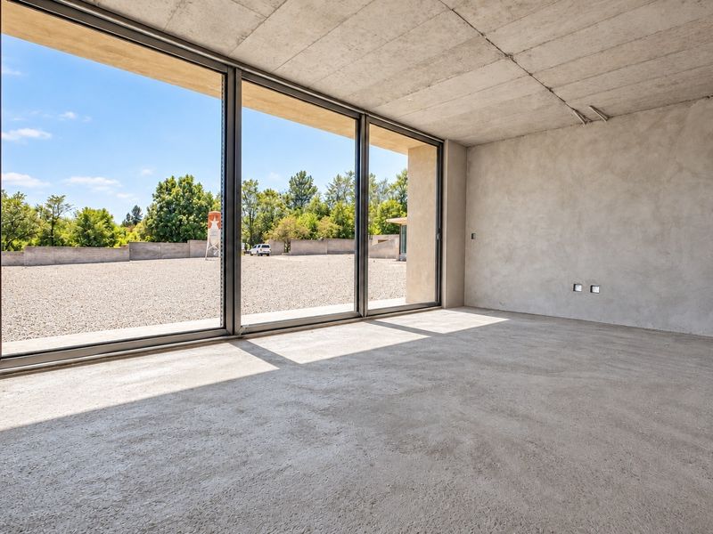 An expansive, unfinished living area featuring raw concrete walls and ceilings with large sliding glass doors opening to an outdoor gravel space.