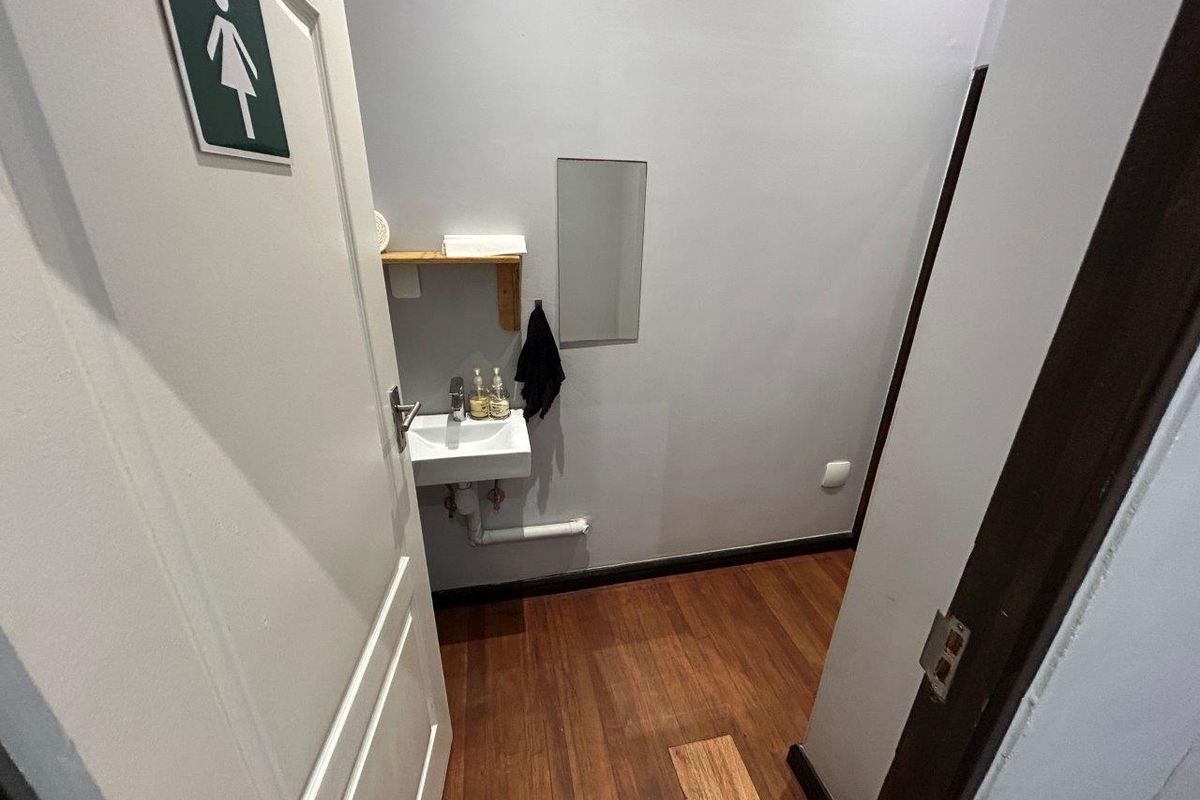 A compact restroom facility featuring a wall-mounted basin, wooden shelving, and timber flooring.
