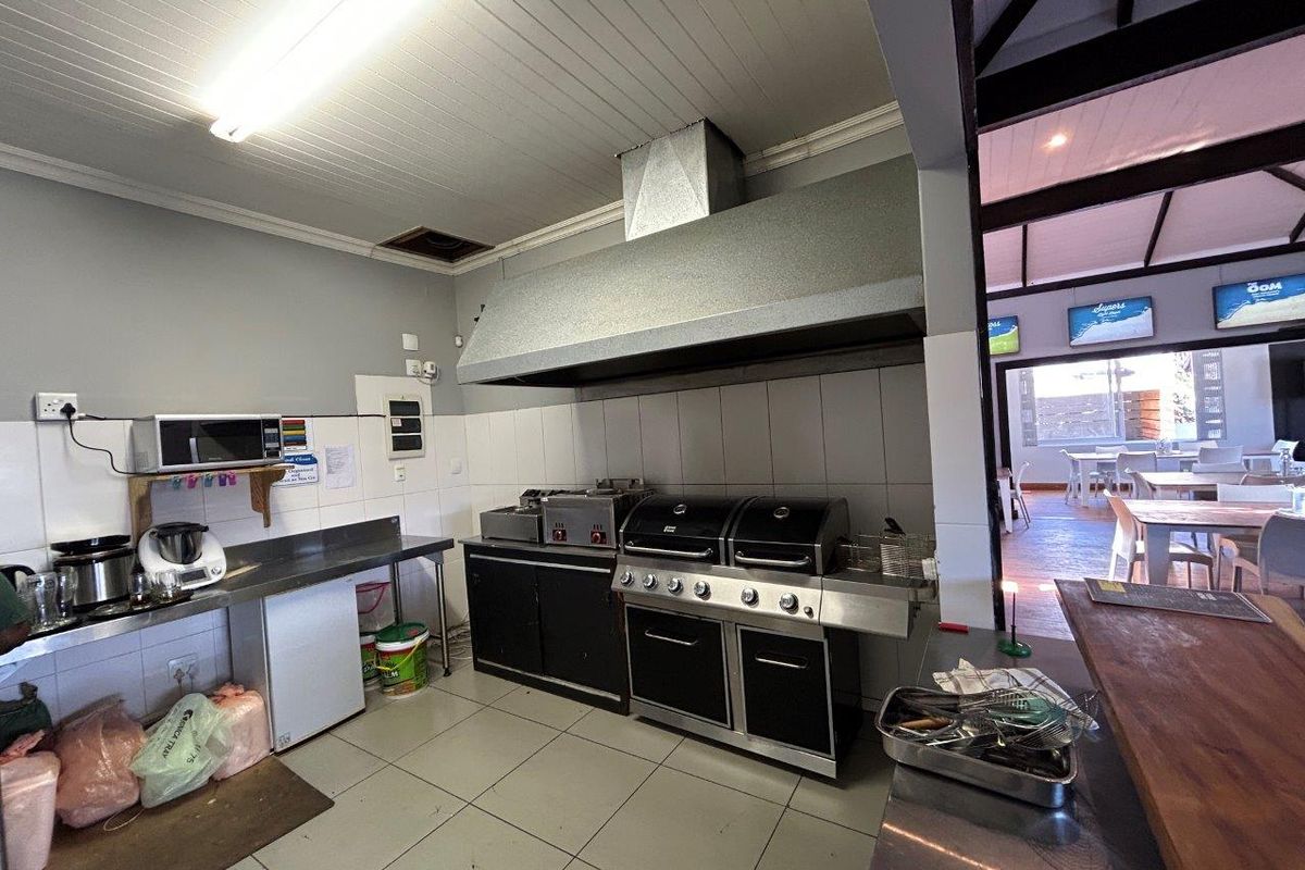 Commercial kitchen area featuring stainless steel prep counters, a large built-in extractor hood, and professional-grade cooking equipment with tiled splashbacks.