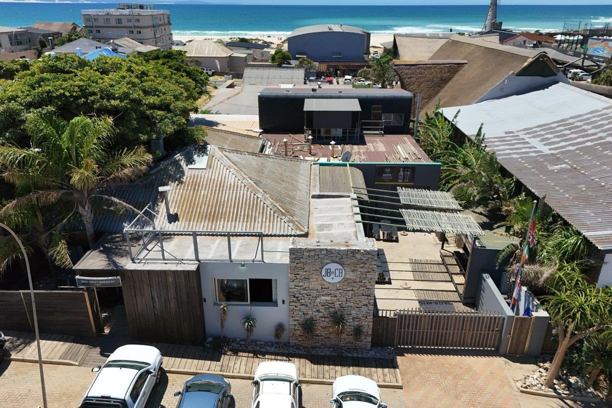 Aerial view of a coastal business property featuring a stone-clad facade, outdoor patio area, and proximity to the beach.