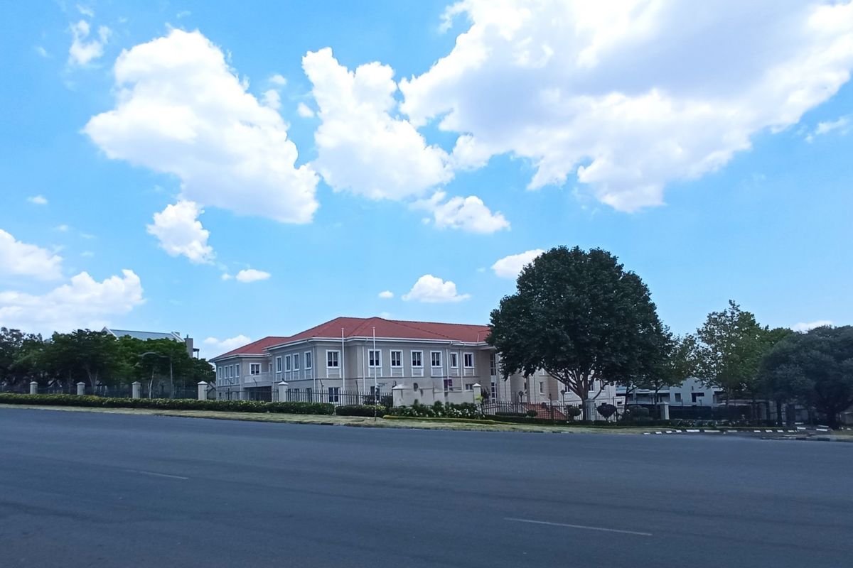 A wide-angle street view of a professional office building complex featuring a tiled roof, multi-pane windows, and secure perimeter fencing.