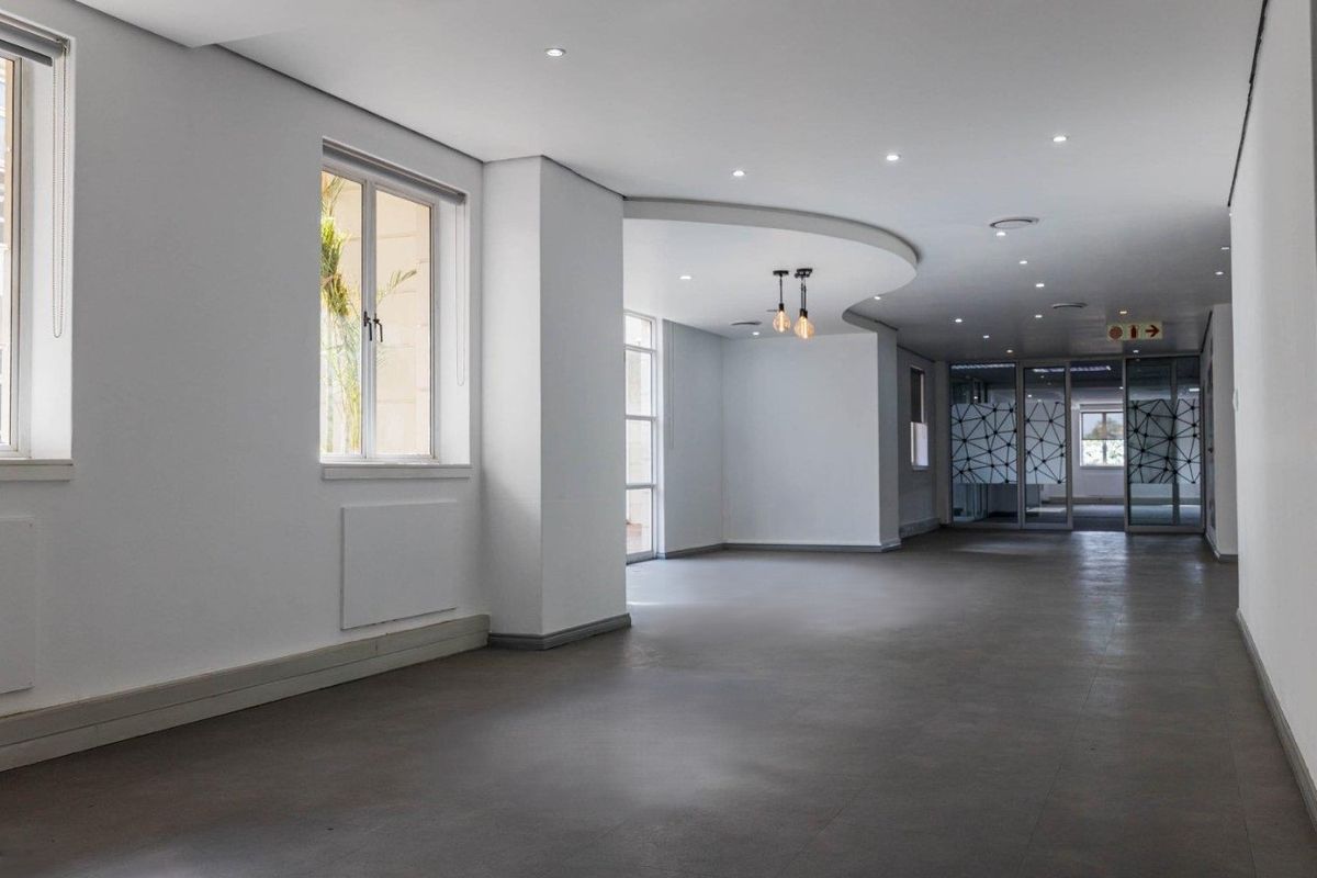 A spacious, open-plan office area featuring modern recessed lighting, a curved ceiling detail, and large windows providing ample natural light.