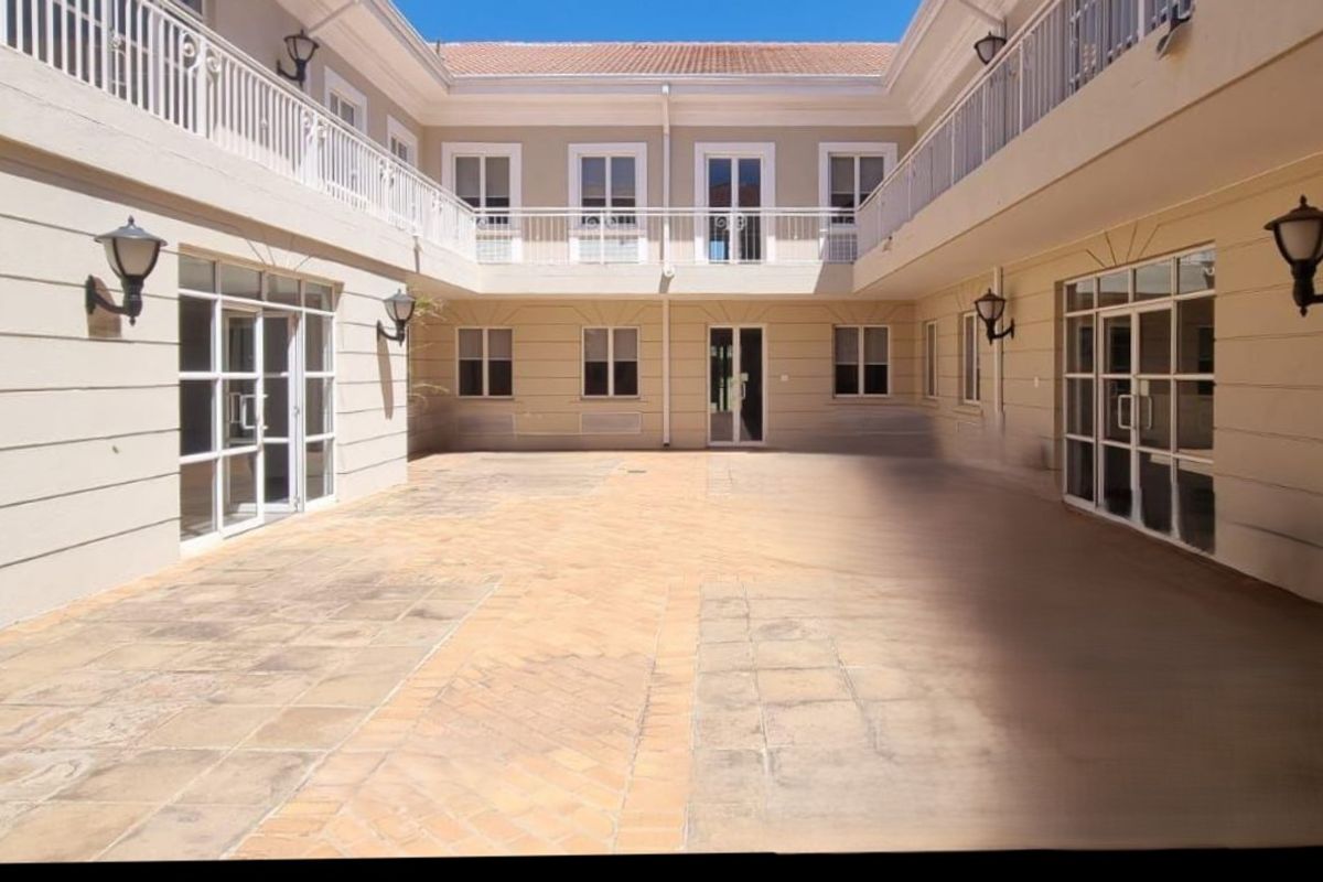 A spacious, paved central courtyard area featuring classic architectural detailing, white railings, and wall-mounted exterior lighting fixtures.