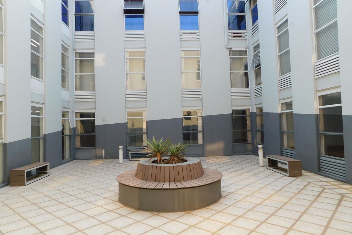 A well-maintained central courtyard featuring tiled flooring, a built-in circular bench with a central planter, surrounded by a multi-story office building facade.