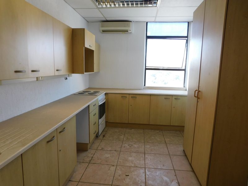 A functional office kitchen featuring light wood-finish cabinetry, an integrated stove and oven, tiled flooring, and a wall-mounted air conditioning unit.