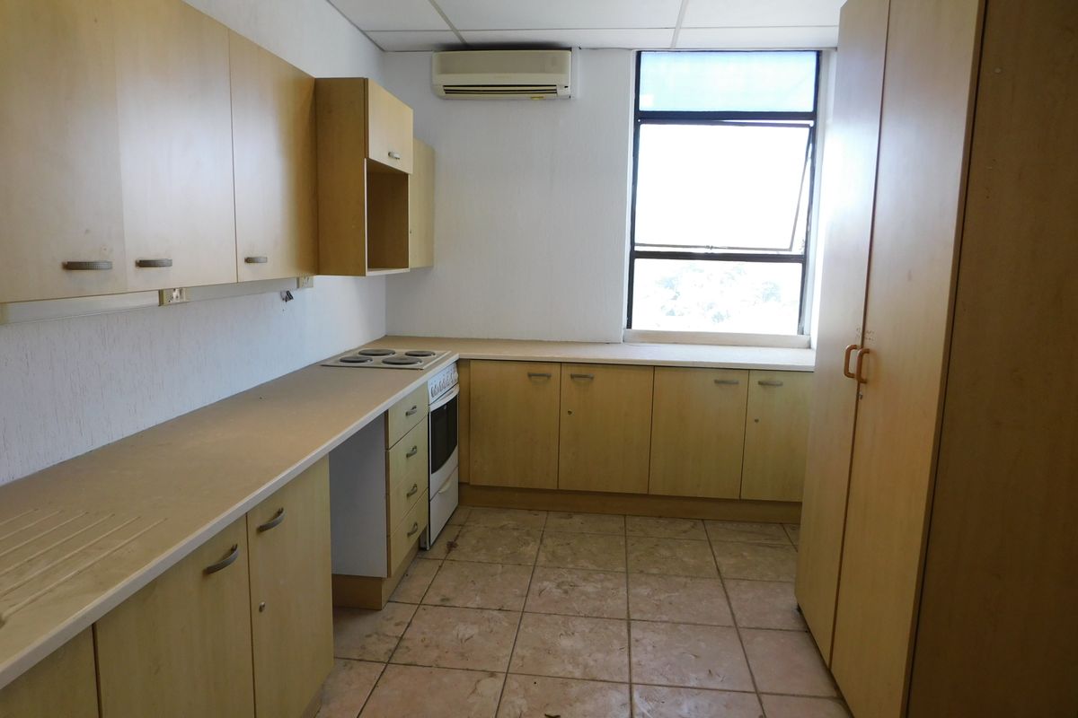 A functional office kitchen featuring light wood-finish cabinetry, an integrated stove and oven, tiled flooring, and a wall-mounted air conditioning unit.