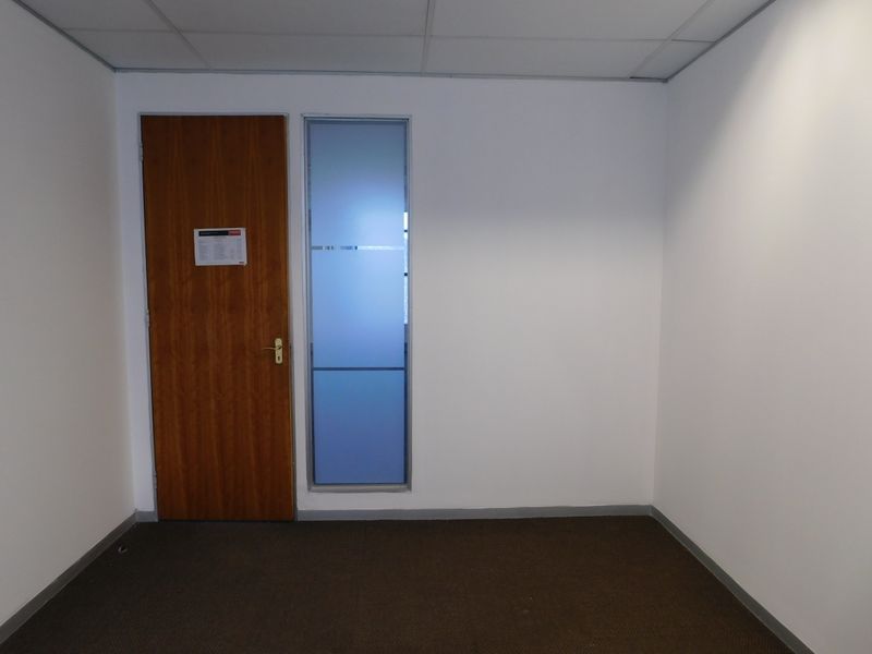 A vacant office space featuring neutral white walls, carpet flooring, a suspended ceiling, and a timber door with an adjacent frosted glass sidelight.