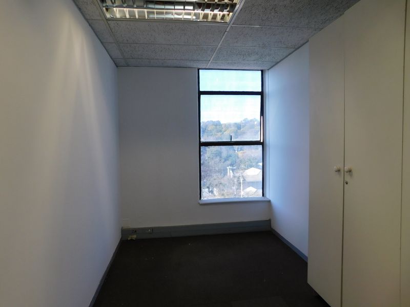 A vacant office space featuring a suspended ceiling, recessed lighting, built-in storage cupboards, and a large window with natural light.