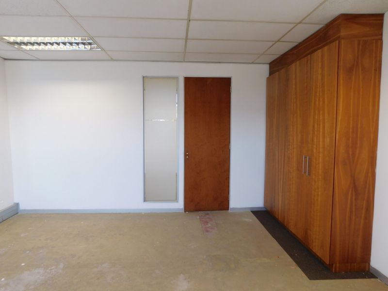 A vacant office space featuring a suspended ceiling, recessed lighting, and extensive built-in wooden cabinetry with a frosted glass sidelight.