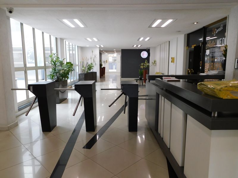 Modern office building entrance featuring security turnstiles, a professional reception desk, and large windows providing ample natural light.