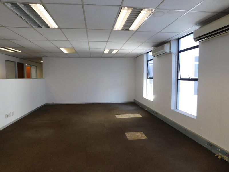An empty office space featuring suspended ceilings, recessed lighting, split-system air conditioning, and carpeted flooring with visible wear.