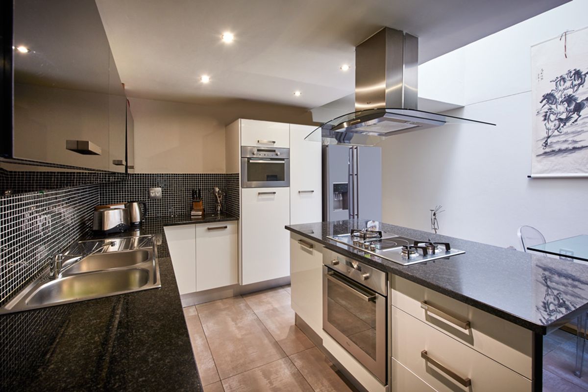 Modern kitchen featuring a central island with a built-in gas hob and oven, stainless steel extractor fan, and sleek cabinetry with granite countertops.
