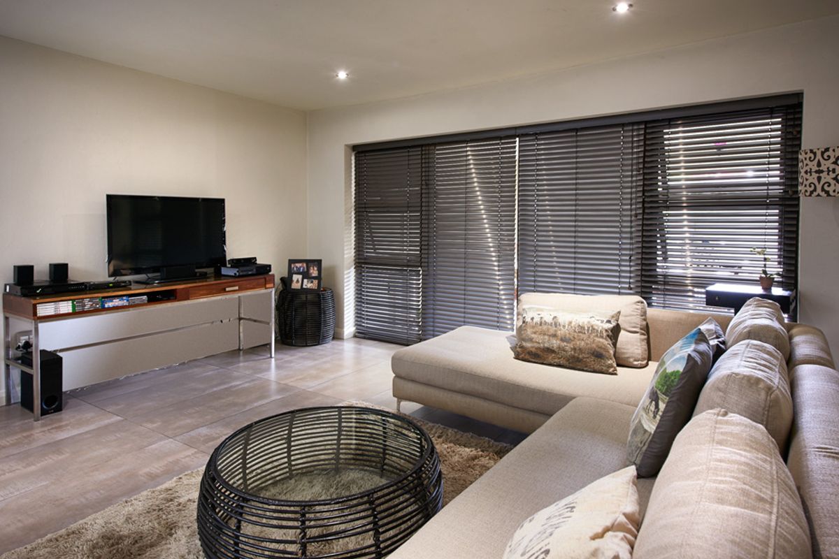 A comfortable living room featuring large sliding glass doors with fitted venetian blinds and modern tiled flooring.