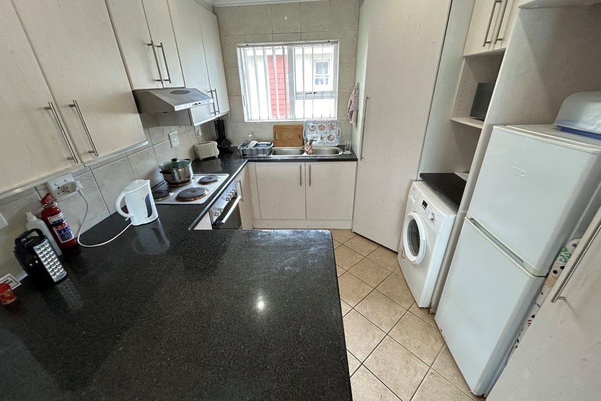 Functional kitchen featuring granite countertops, built-in cabinetry, electric hob, oven, and integrated laundry plumbing, offering a practical layout for daily use.
