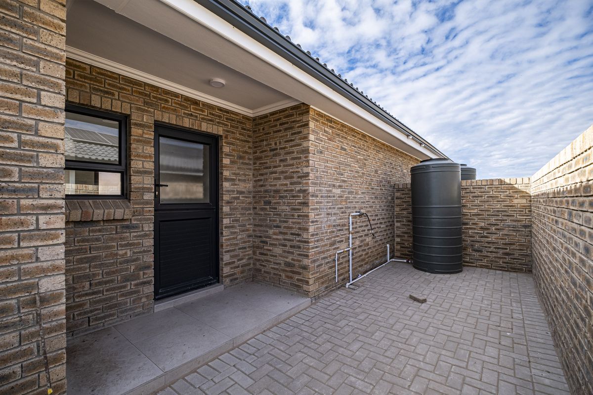 A private rear courtyard featuring face-brick walls, paved flooring, a water storage tank, and direct access to the home via a secure door.