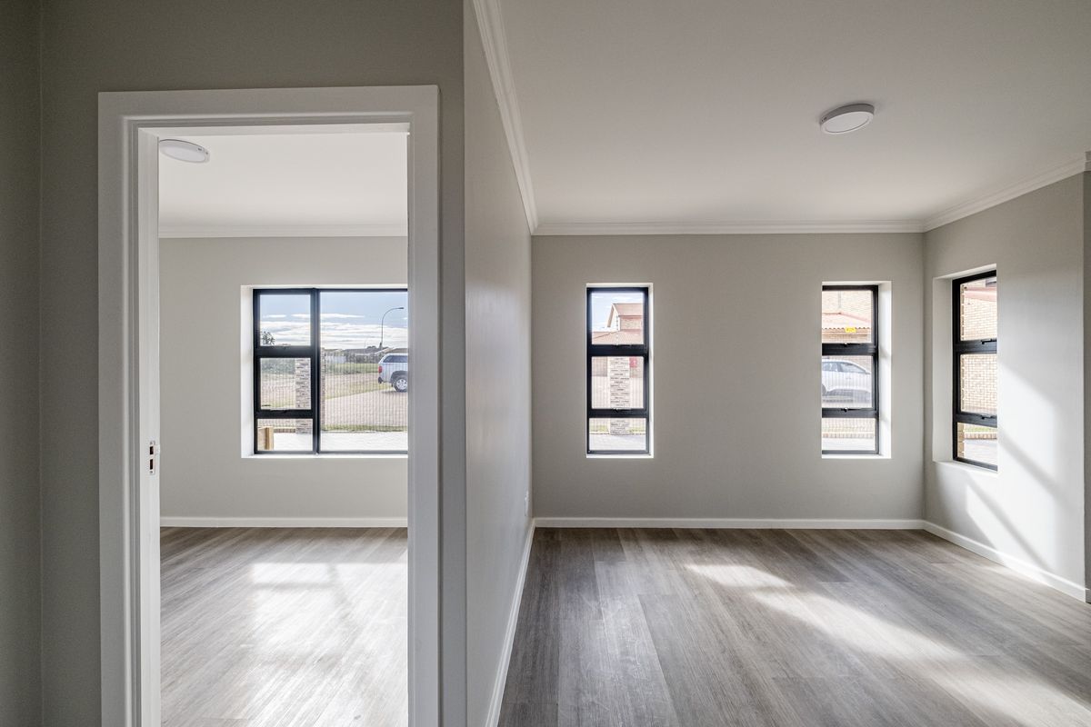 Bright and modern living area featuring neutral grey walls, wood-look laminate flooring, and contemporary black-framed windows providing ample natural light.