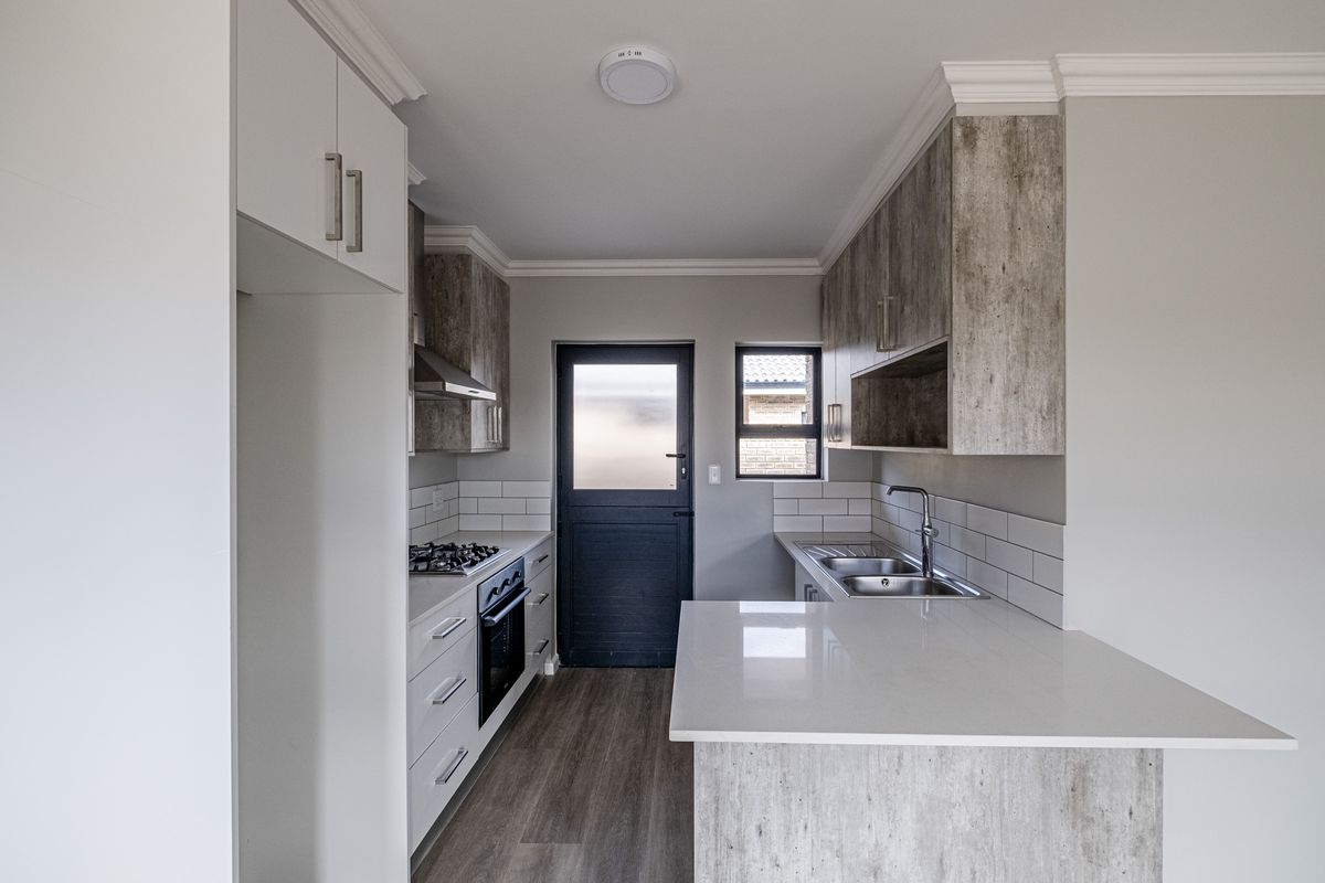 Modern kitchen featuring stone countertops, built-in gas hob, oven, extractor fan, and double stainless steel sink with contemporary cabinetry.